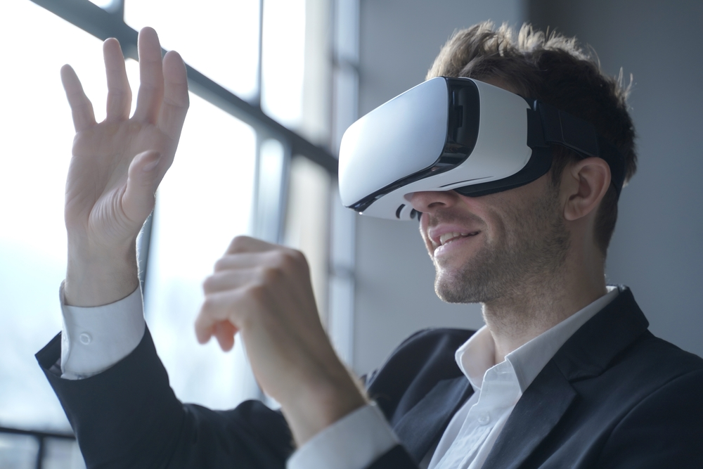 European man office employee wears formal suit and VR headset glasses excited of experiencing virtual reality stretching his hands up trying to catch seemingly round object totally immersed in 3D game.