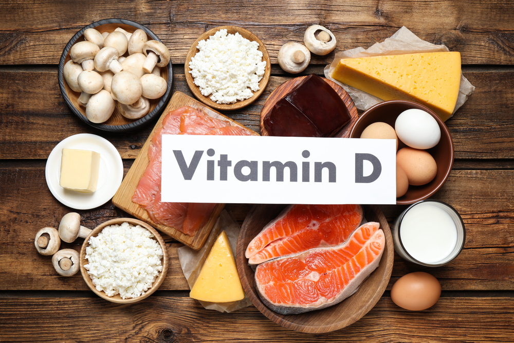 An assortment of foods rich in Vitamin D, including mushrooms, cheese, eggs, milk, salmon, and butter, with a sign labeled 